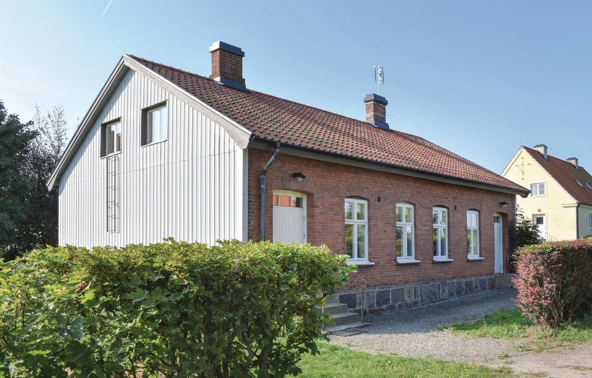 Een huis met twee verdiepingen, een dak met rode tegels, witte gevelbekleding en een bakstenen schoorsteen.