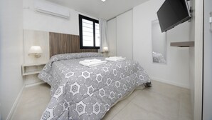 Ett modernt sovrum med en säng, sänglampor, en TV som är monterad på väggen och en luftkonditioneringsanläggning.
