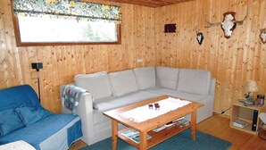 Ein Zimmer mit Holzwänden, einem weißen Sofa, einem blauen Sessel, einem Holztisch und einem Fenster mit einem Blumenvorhang.