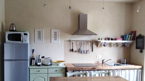 A kitchen with a wooden table, chairs, a microwave, a refrigerator, and a hanging pot rack.