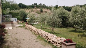 A garden pathway leading to a house with a white fence, stone wall, and a small structure in the background.