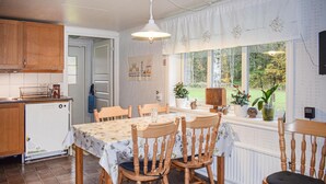 En matplats med ett bord för fyra personer, trästolar, ett fönster med utsikt över grönområden och ett köksområde med skåp och diskmaskin.