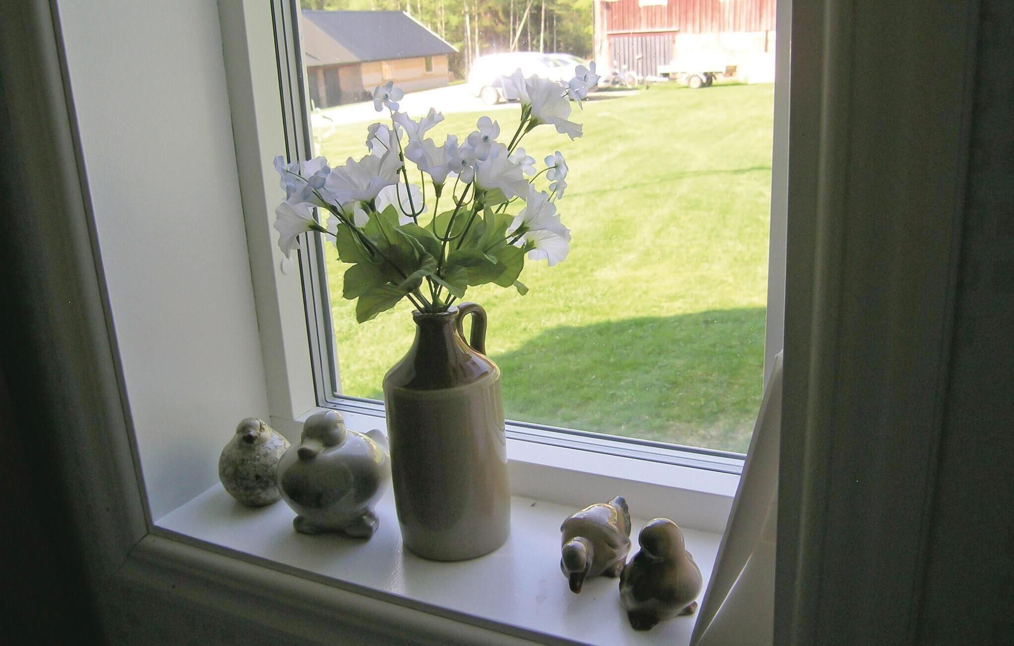 A window with a vase of white flowers, a ceramic bird, and a ceramic turtle on the sill.