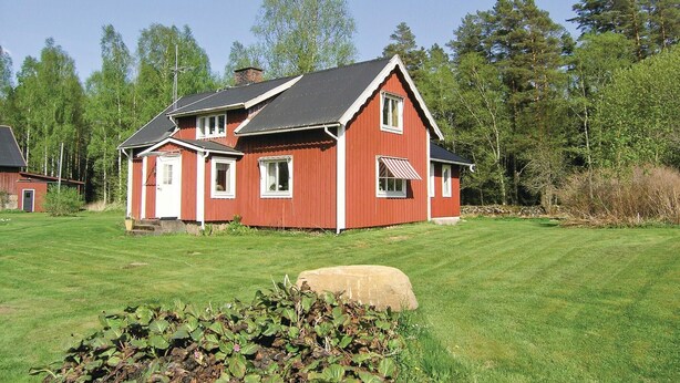 Ett rött hus med ett sluttande tak, en veranda och en stor sten i förgrunden.