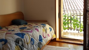 Een slaapkamer met een bed, een kleedje, een foto aan de muur en uitzicht op een balkon met een betegeld dak.