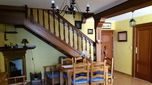 Een trap met houten leuningen en een kroonluchter, die leidt naar een ruimte met een eettafel en stoelen.