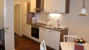 Eine kompakte Küche mit weißen Schränken, einem schwarzen Backofen, einer Edelstahl-Spüle und einer Holz Arbeitsplatte.