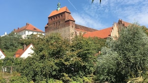Ein historisches Gebäude mit einem markanten Turm und roten Ziegeldächern, umgeben von üppiger Vegetation.
