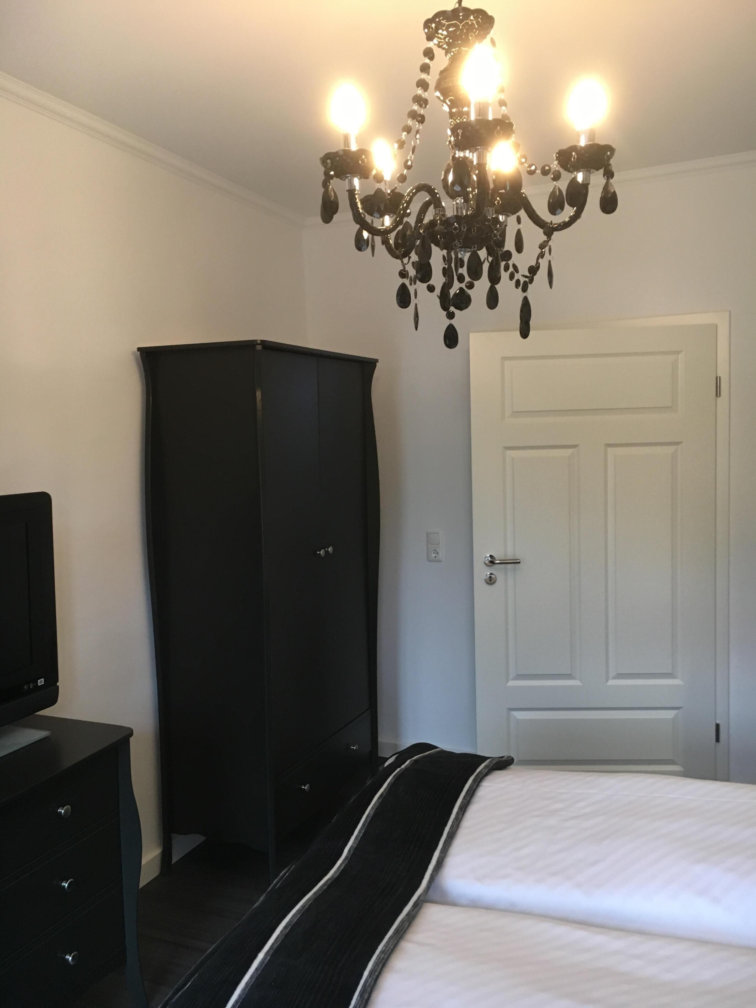 A bedroom with a bed, a wardrobe, a television, and a chandelier.