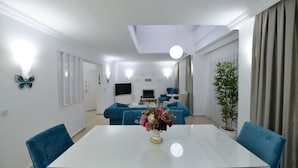 A modern living room with a glass dining table, blue sofas, and a potted plant. - 3 bedroom luxury villa in ovacik oludeniz for rent (fethiye)