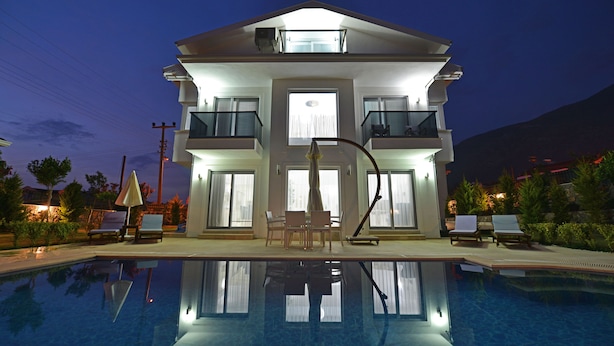 A modern multi-story hotel with a swimming pool, outdoor seating, and balconies. - 3 bedroom luxury villa in ovacik oludeniz for rent (fethiye)