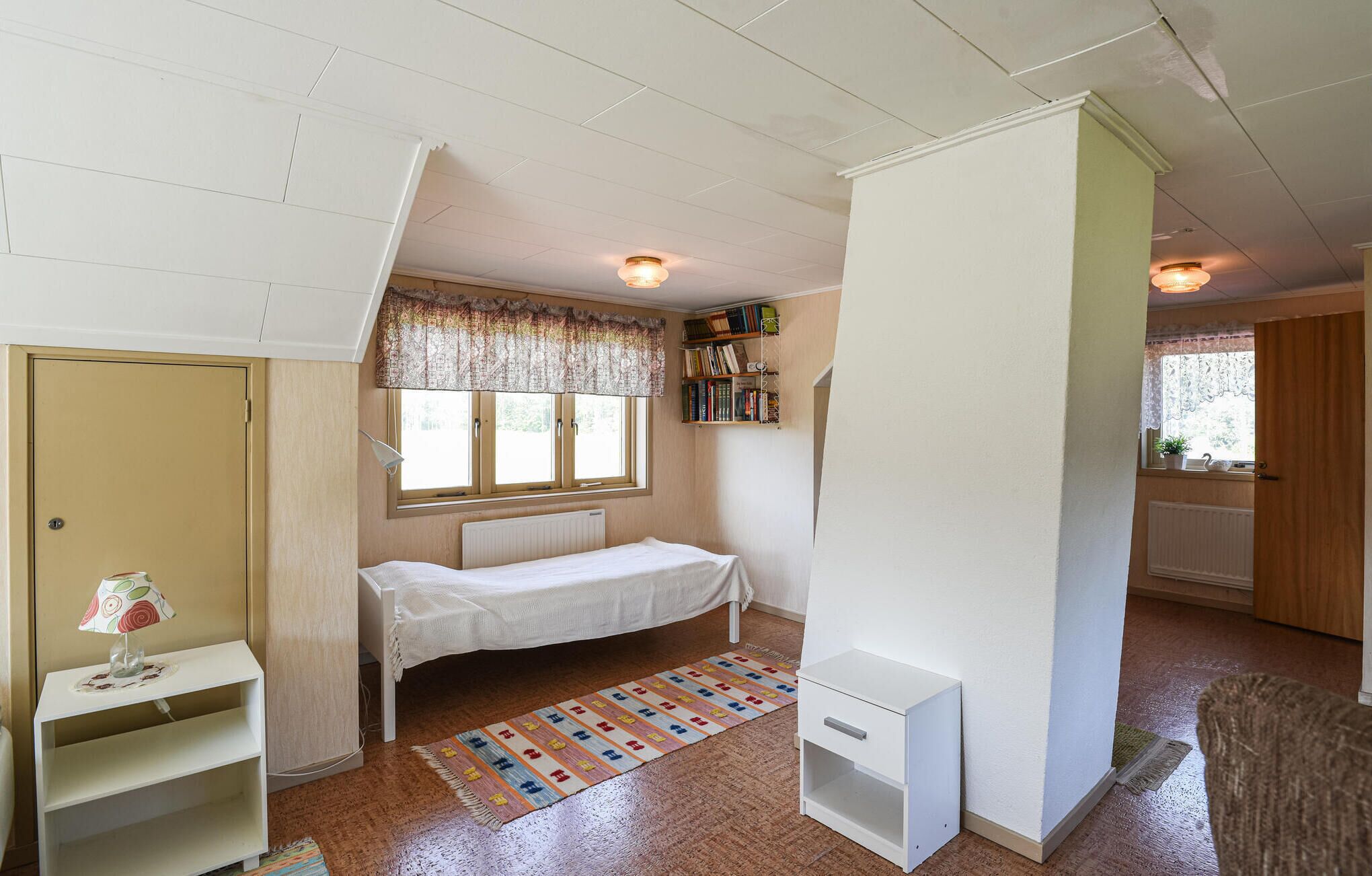 Una habitación pequeña y bien iluminada con una cama individual, una estantería y un radiador.