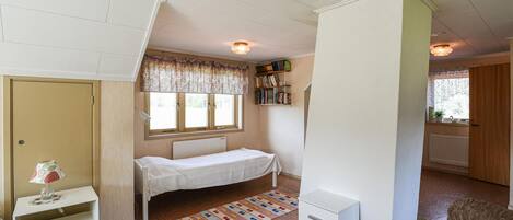 Una habitación pequeña y bien iluminada con una cama individual, una estantería y un radiador.