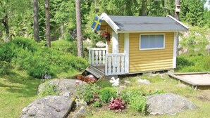 A small wooden cabin with a porch, surrounded by lush greenery and rocks. - Lovely home in Tived with WiFi (Tived)