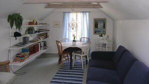 Et hyggeligt loftsværelse med spisebord, stole, reol, sofa og en lysekrone.