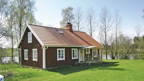 Et træhus med rødt tegltag, en veranda og en græsplæde.