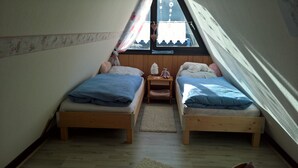 A small attic bedroom with two wooden beds, a wooden nightstand, and a window with a view of the outside. - Holiday house Fichtelgebirgshaus (Hüttstadl)