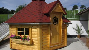 A small wooden cabin with a red roof, a window with a flower box, and a door with a decorative panel. - New vacation home with indoor pool in the beautiful Thuringian Forest on the Rennsteig (Trusetal)