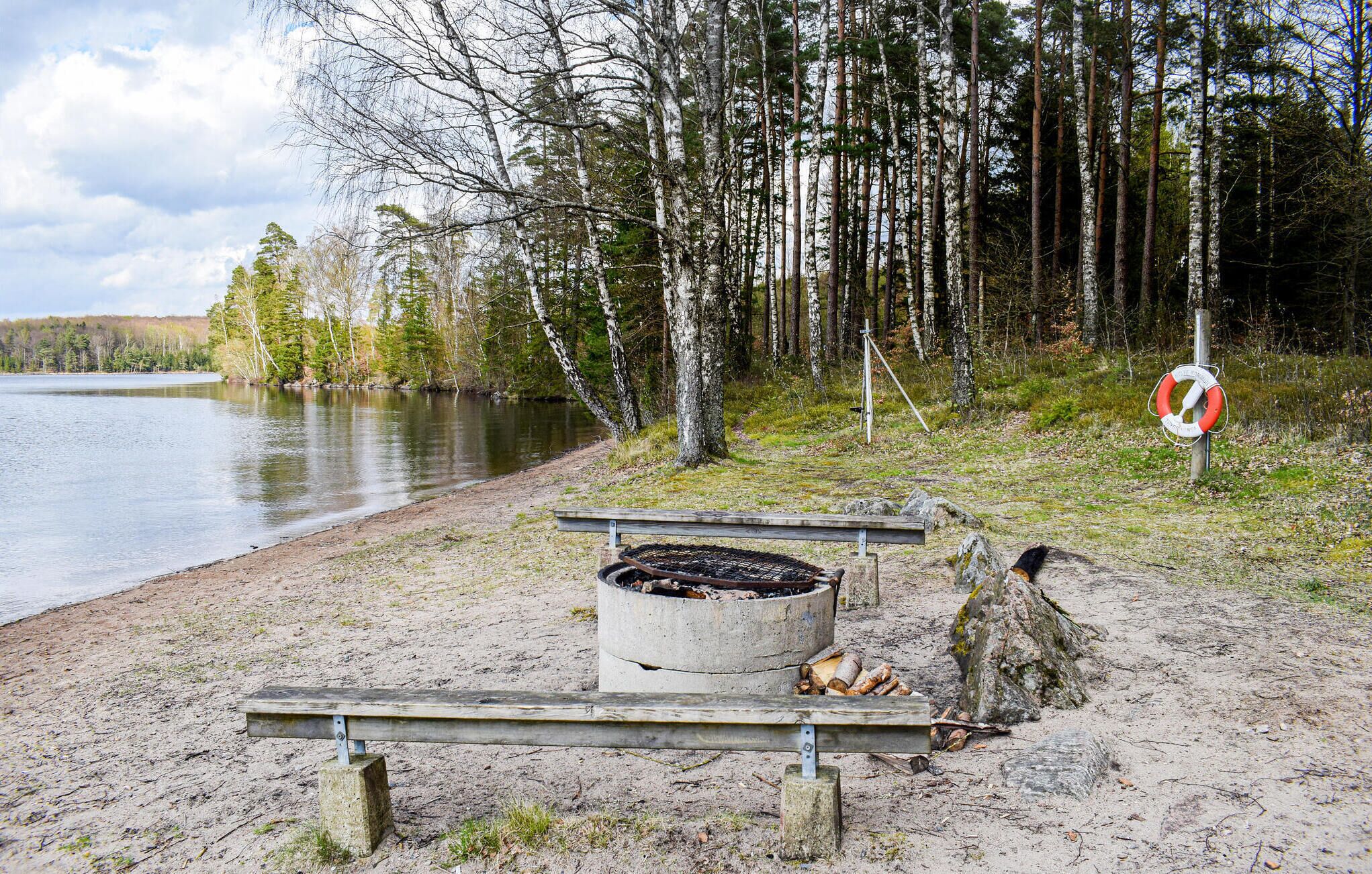A lakeside campsite with a fire pit, benches, and a lifebuoy on a pole.