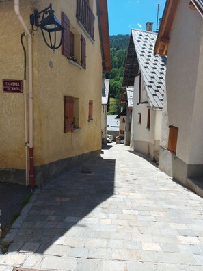 Une étroite rue pavée bordée de bâtiments à l’architecture européenne traditionnelle, dont un panneau indiquant « TRAVERSE du MAIT ».