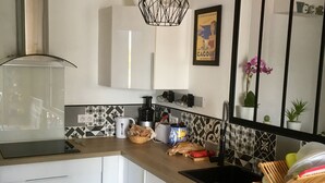 Una cocina moderna con armarios blancos, encimera de madera y salpicadero negro. Se aprecia una campana extractora de acero inoxidable, una lámpara colgante y una planta en maceta.