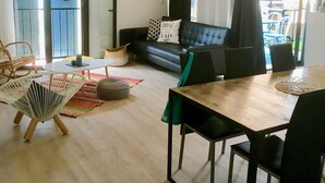 Una sala moderna con un sofá negro, una mesa de comedor con sillas, una lámpara colgante y vistas a través de un ventanal.