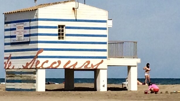 Una pequeña cabaña de playa a rayas con un letrero que dice "Le Secours".