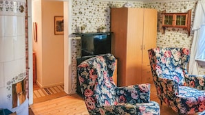 Una habitació amb terres de fusta, televisió, armari i cadires amb motius florals.