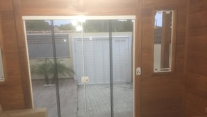 A room with a sliding glass door leading to an outdoor area with a patio and a white garage door. - Bangalôs do Parque (Penha)