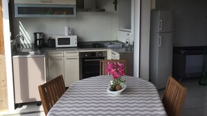A compact kitchen with a microwave, stove, and sink. There's a dining table with chairs and a vase of flowers.