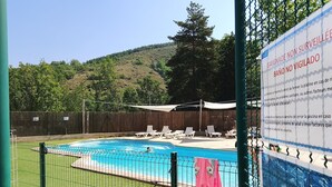 Ein Schwimmbecken mit umzäuntem Bereich, Liegestühlen und einem Schild, das darauf hinweist, dass keine Aufsichtsperson anwesend ist.