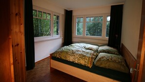 Une chambre à coucher avec un lit en bois, de grandes fenêtres et une vue sur les arbres.