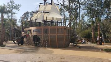 A wooden pirate ship structure with a flag, surrounded by trees and a sandy ground.