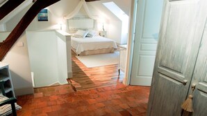 A bedroom with a sloped ceiling, a bed with a canopy, a wooden floor, and a door leading to another room. - Charming and Chic Vineyard House (SAINT ROMAIN)