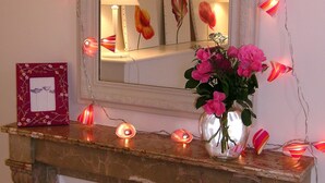 A mirror with a floral frame, a vase with pink flowers, and decorative lights on a mantelpiece. - Charming and Chic Vineyard House (SAINT ROMAIN)
