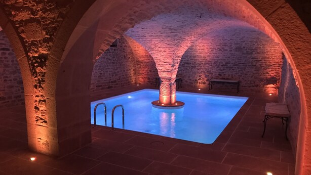 A stone-walled indoor swimming pool with a central column, surrounded by arches and stone walls. - Charming and Chic Vineyard House (SAINT ROMAIN)