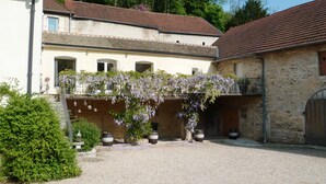 A courtyard with a gravel ground, a building with a tiled roof, and a vine-covered wall. - Charming and Chic Vineyard House (SAINT ROMAIN)