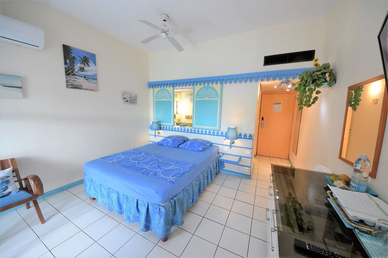 Une chambre à coucher comprenant un lit, un bureau, une chaise, un ventilateur de plafond et une porte donnant sur une autre pièce.