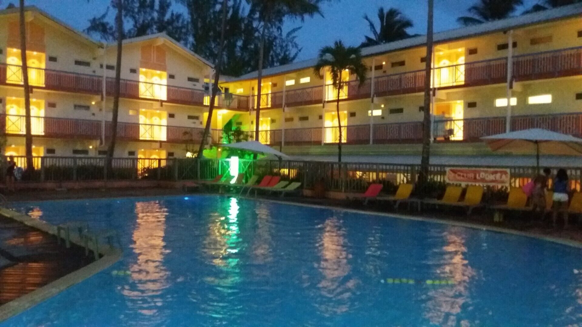A hotel with a swimming pool, multiple balconies, and a brightly lit facade.