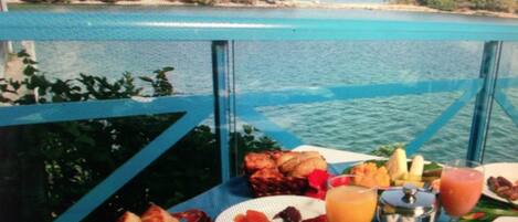 A table with breakfast items including fruits, a drink, and a cup of coffee, overlooking a body of water.