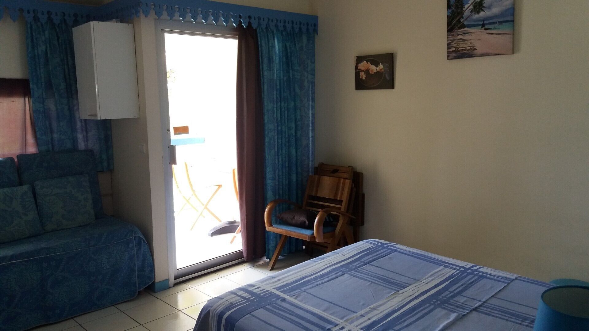 A room with a bed, a chair, a sofa, and a window with curtains.