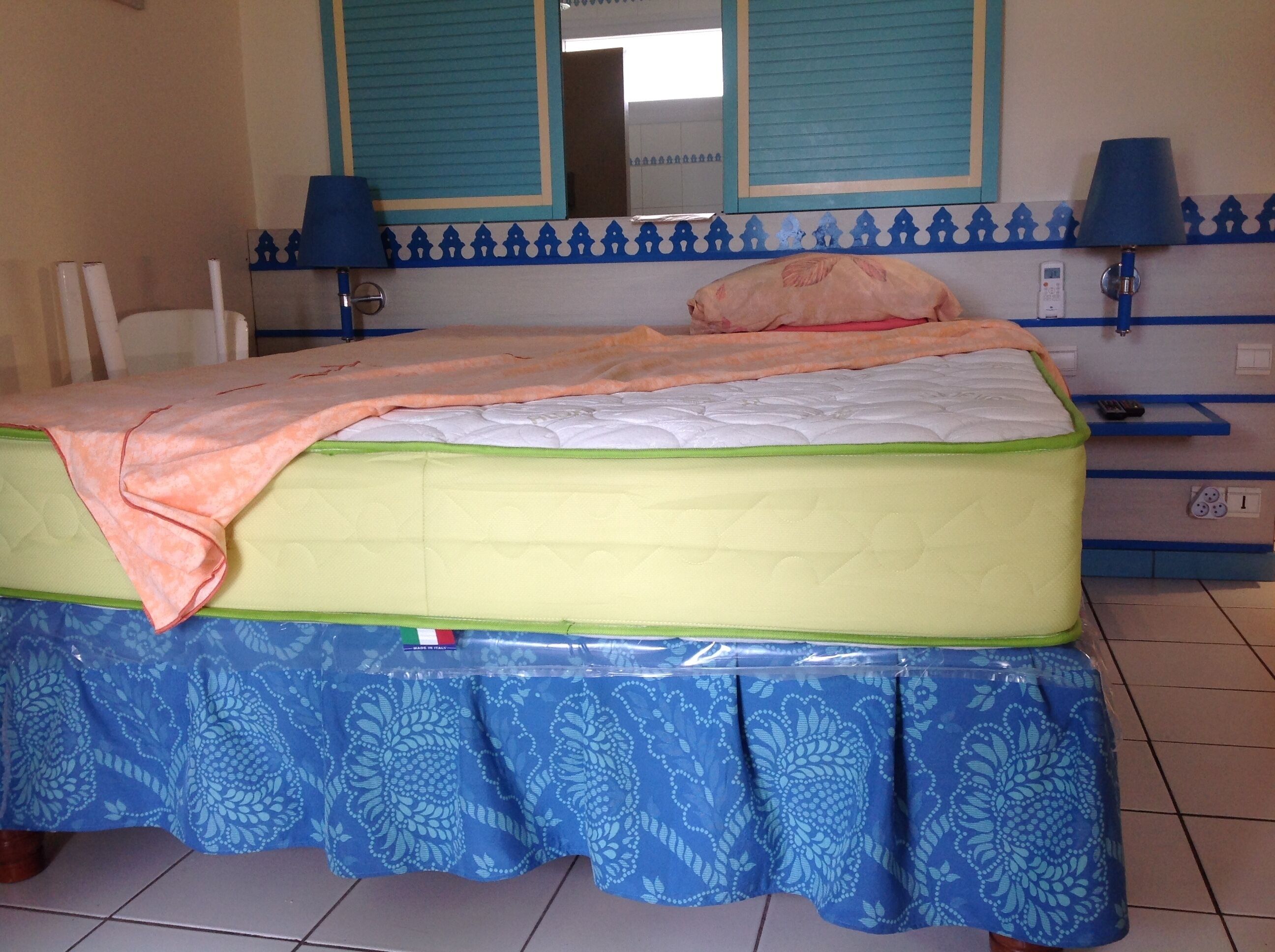 Een bed met een bedrok met patroon, een nachtkastje met een lamp, en een muur met decoratieve rand.