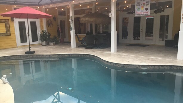 An indoor swimming pool with a red umbrella, a thatched roof, and a sign for a bar.