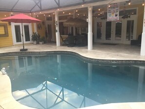 Una piscina interior con una sombrilla roja, techo de paja y un cartel para un bar.