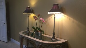 A glass-top console table with two lamps and a potted orchid plant.