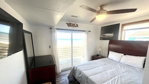 A hotel room with a bed, a ceiling fan, a window with curtains, and a view of the beach.
