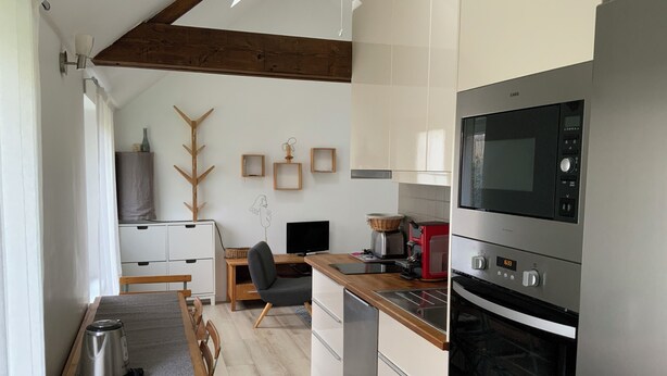 A modern kitchen with a built-in microwave, oven, and coffee maker. There is a dining table with chairs, a wooden chair, and a small rug on the floor. - Maisonnette de Senlis rated 3*. Calm and excellent comfort (Senlis)