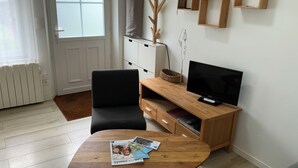 A living room with a wooden coffee table, a black sofa, a TV on a wooden stand, and a white radiator. - Maisonnette de Senlis rated 3*. Calm and excellent comfort (Senlis)