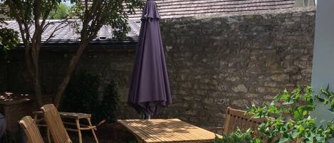 An outdoor patio with wooden furniture, including a table and chairs, and a purple umbrella.