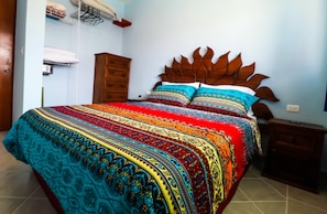 A bed with a patterned bedspread, a wooden headboard, and a nightstand with a lamp. - Fully Equipped Art Loft- Bicycles & Snorkel Gear - Corpus Christi -Extras (Cozumel)
